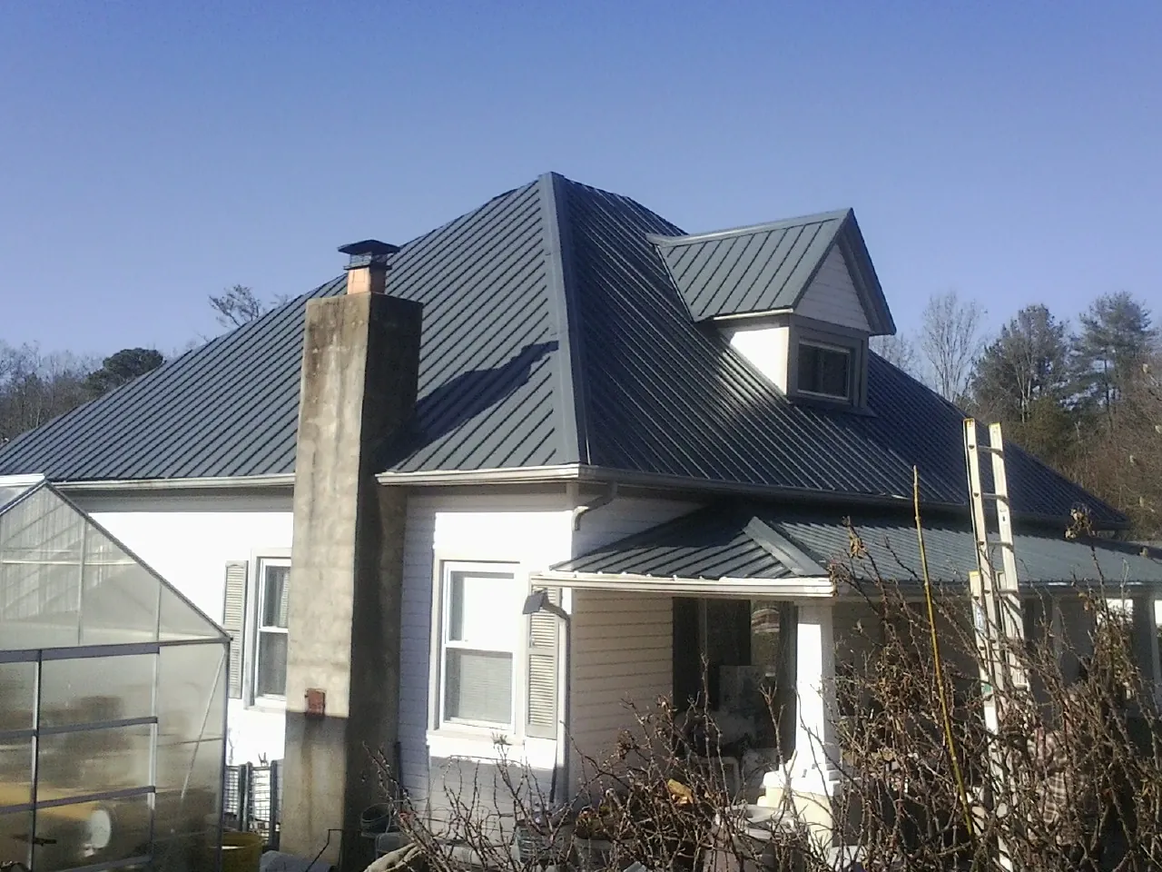 Dark blue standing seam metal roof on a white farmhouse with dormer — Slate & Tile Roof Repair by Roofing Brothers in Seth
