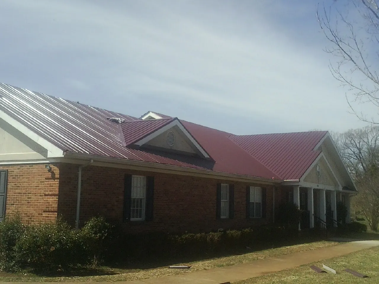 Red metal roof with gabled entries on a long brick building, from a Hail Damage Roof Repair job in Seth