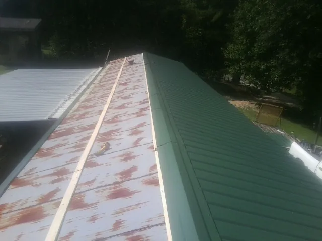 Old rusted panels beside newly installed green metal roofing — Wind Damage Roof Repair by Roofing Brothers in Seth