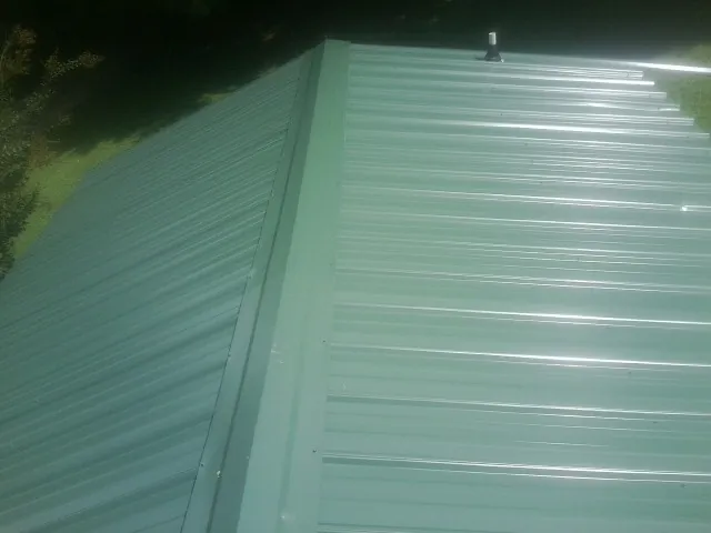 New green metal panels meeting at the ridge of a roof — Flat Roof Repair work by our crew in Seth