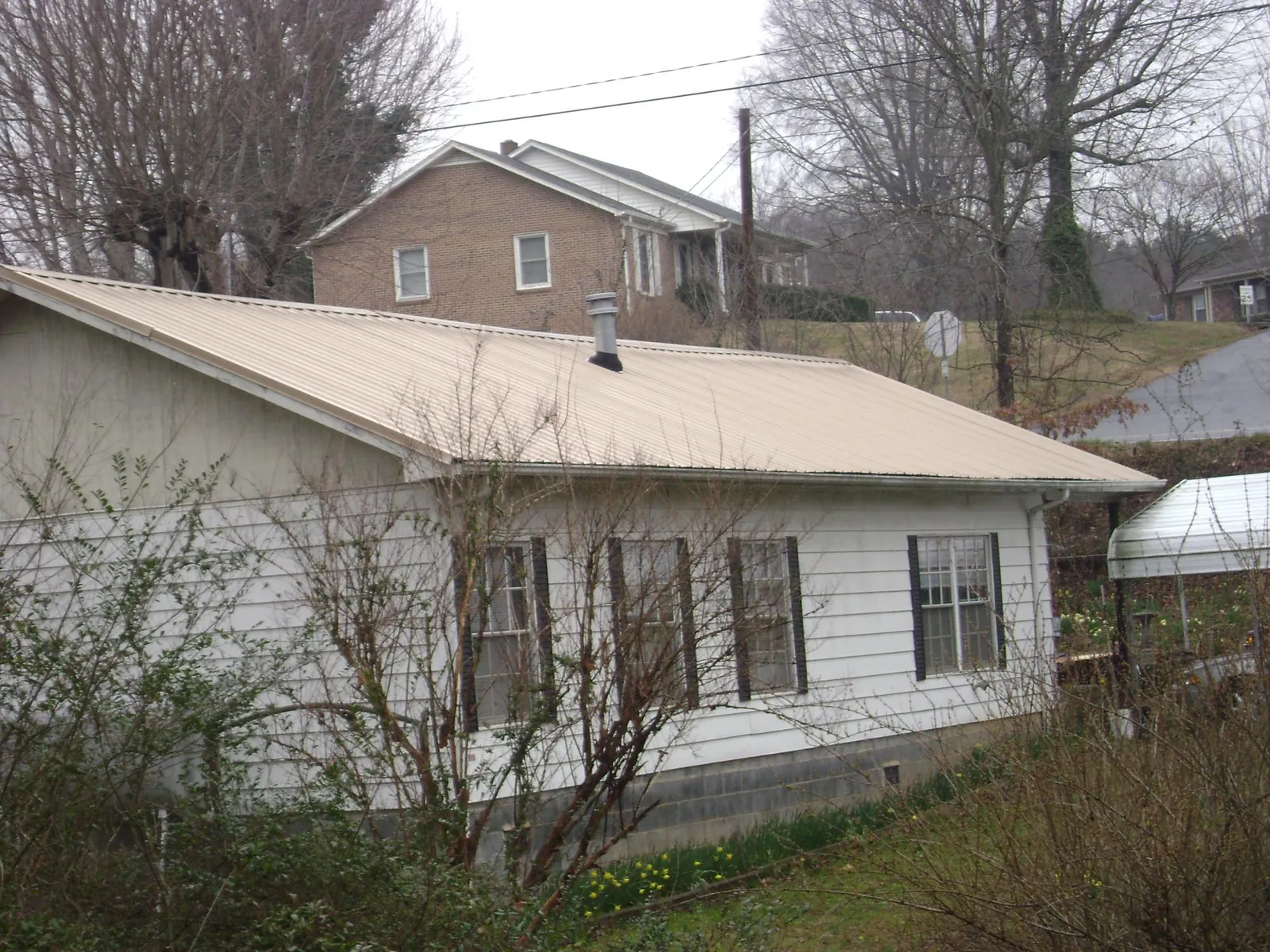 Tan metal roof on a white sided house set into a hillside — Commercial Roofing by Roofing Brothers in Seth
